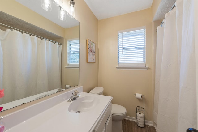 bathroom with plenty of natural light, wood finished floors, toilet, and baseboards