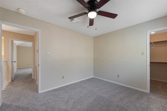 unfurnished bedroom with carpet, visible vents, a spacious closet, a textured ceiling, and baseboards