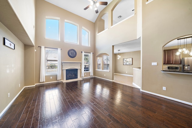 unfurnished living room with baseboards, ceiling fan with notable chandelier, hardwood / wood-style floors, and a glass covered fireplace