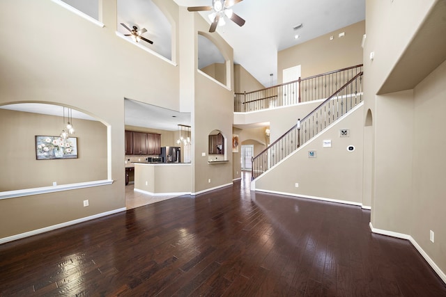 unfurnished living room featuring baseboards, arched walkways, hardwood / wood-style flooring, stairway, and ceiling fan with notable chandelier