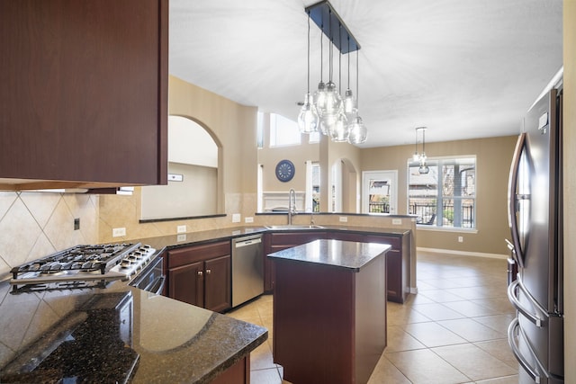 kitchen featuring decorative backsplash, appliances with stainless steel finishes, dark stone countertops, a peninsula, and a sink