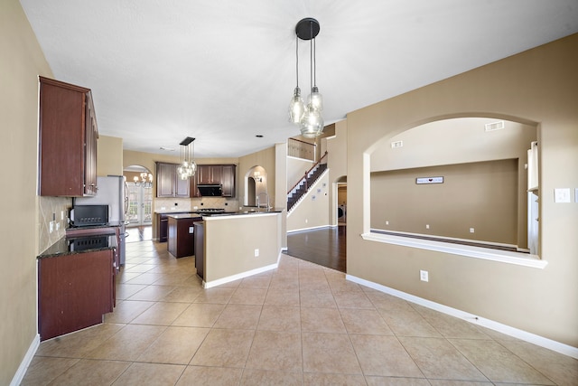 kitchen with light tile patterned floors, a center island with sink, visible vents, decorative light fixtures, and backsplash