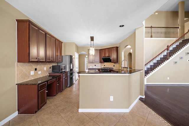 kitchen featuring arched walkways, light tile patterned floors, stainless steel microwave, a peninsula, and baseboards