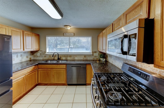 kitchen featuring tasteful backsplash, dark stone counters, stainless steel appliances, a sink, and light tile patterned flooring