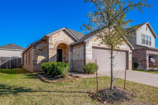 french country style house with an attached garage, fence, stone siding, driveway, and a front lawn