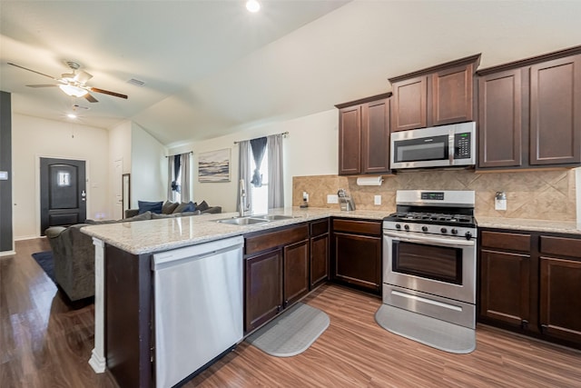 kitchen with stainless steel appliances, open floor plan, a sink, dark brown cabinetry, and a peninsula