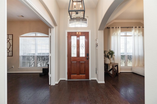 foyer with arched walkways, plenty of natural light, baseboards, and wood finished floors