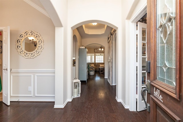 hall featuring arched walkways, dark wood-style flooring, baseboards, and a decorative wall