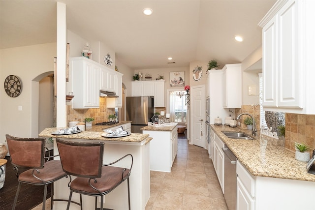 kitchen featuring a peninsula, a sink, white cabinets, appliances with stainless steel finishes, and light stone countertops