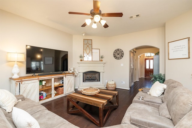 living room featuring arched walkways, visible vents, a fireplace with raised hearth, ceiling fan, and wood finished floors