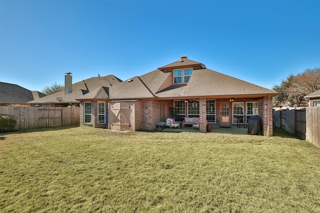 back of property featuring brick siding, a patio, a shingled roof, a lawn, and a fenced backyard