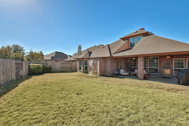 rear view of property featuring a patio, a fenced backyard, roof with shingles, a yard, and brick siding