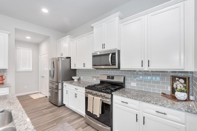 kitchen featuring white cabinets, light wood-style flooring, stainless steel appliances, and backsplash