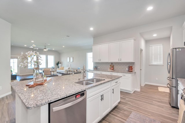 kitchen with light wood-style flooring, a sink, appliances with stainless steel finishes, backsplash, and an island with sink