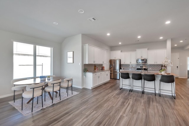 kitchen with tasteful backsplash, visible vents, appliances with stainless steel finishes, white cabinetry, and wood finished floors