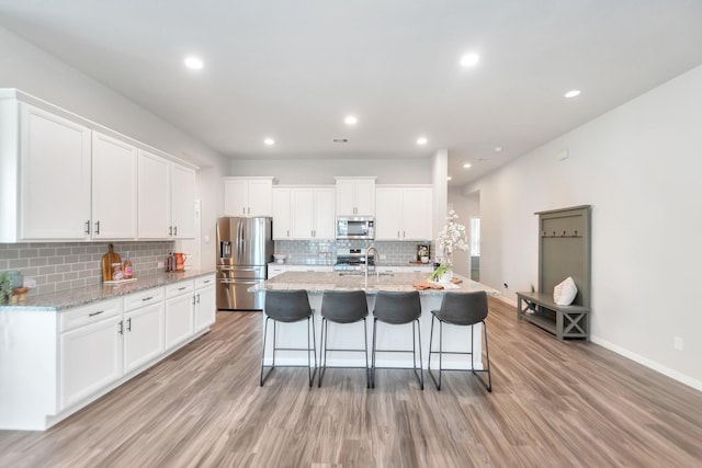 kitchen with appliances with stainless steel finishes, white cabinets, a sink, and light wood-style flooring