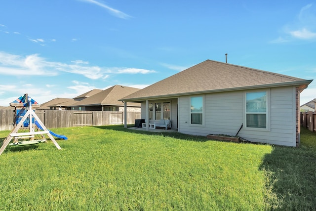 rear view of house featuring a fenced backyard, a shingled roof, a lawn, and a playground