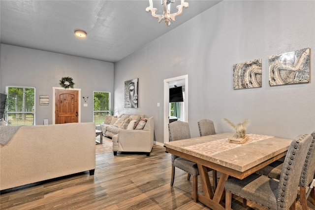 dining space featuring a towering ceiling, wood finished floors, a wealth of natural light, and a notable chandelier