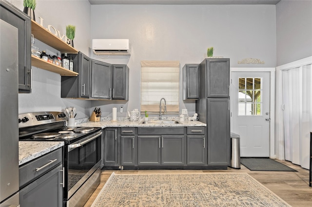 kitchen with light wood finished floors, stainless steel electric range oven, light stone countertops, a sink, and a wall mounted AC