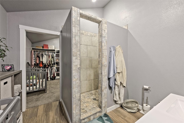 bathroom featuring vaulted ceiling, a spacious closet, walk in shower, and wood finished floors