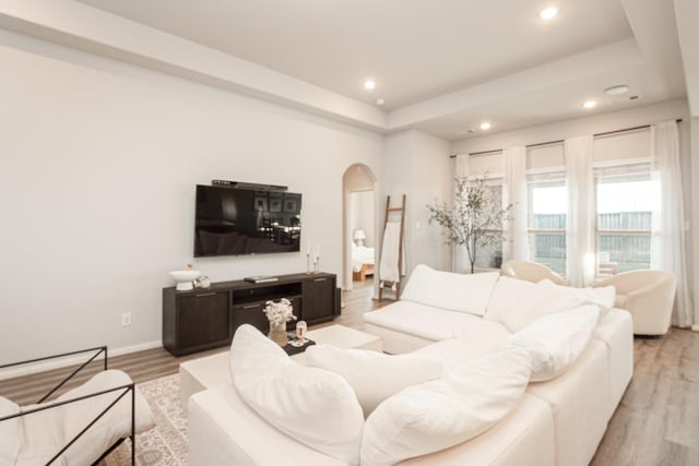 living area with light wood-type flooring, arched walkways, a tray ceiling, and recessed lighting