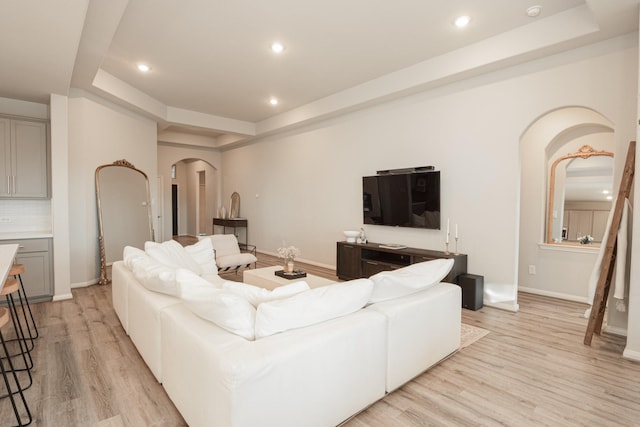 living area with light wood-type flooring, arched walkways, and a tray ceiling