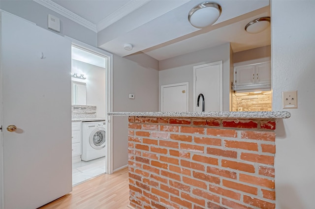 kitchen featuring a sink, white cabinetry, light wood-type flooring, washer / dryer, and crown molding