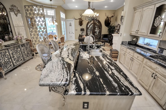 kitchen featuring a spacious island, ornamental molding, dark stone countertops, decorative light fixtures, and a sink