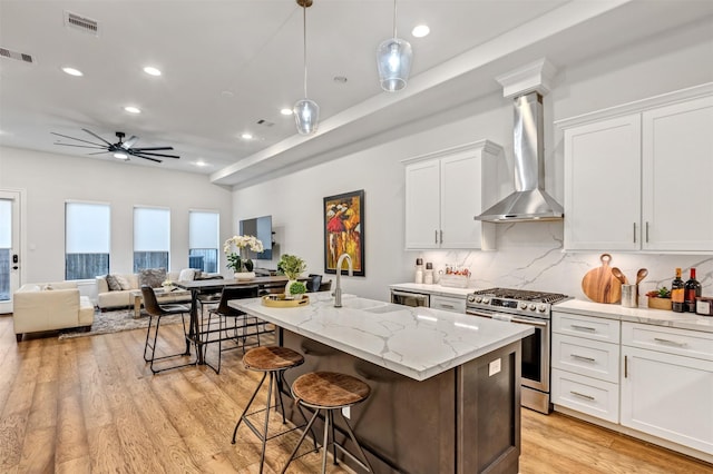 kitchen featuring light wood finished floors, stainless steel gas range oven, visible vents, wall chimney exhaust hood, and a sink