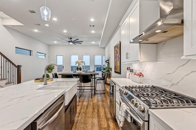 kitchen featuring visible vents, appliances with stainless steel finishes, white cabinetry, wood finished floors, and wall chimney exhaust hood