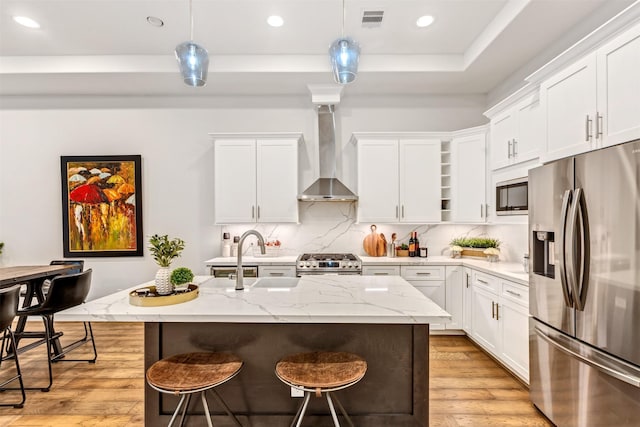 kitchen with light wood finished floors, visible vents, appliances with stainless steel finishes, a sink, and wall chimney range hood