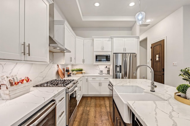 kitchen with decorative backsplash, appliances with stainless steel finishes, dark wood-type flooring, white cabinetry, and wall chimney range hood