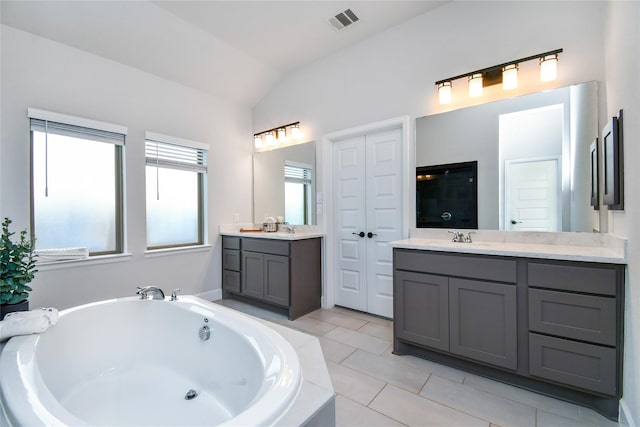 bathroom with visible vents, lofted ceiling, a bath, tile patterned flooring, and a sink