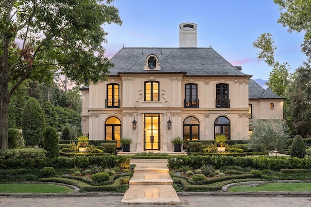 french provincial home featuring french doors, a chimney, a high end roof, and stucco siding