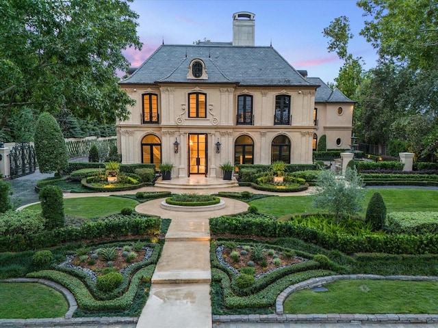 french country home featuring a high end roof, fence, a chimney, and stucco siding