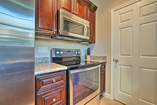 kitchen with appliances with stainless steel finishes, light tile patterned floors, baseboards, and light stone countertops