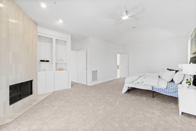 carpeted bedroom featuring a tiled fireplace, visible vents, ceiling fan, and vaulted ceiling