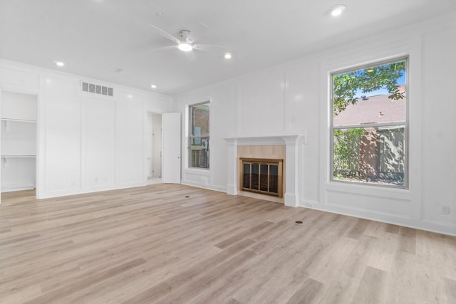 unfurnished living room featuring a decorative wall, visible vents, a ceiling fan, and a glass covered fireplace