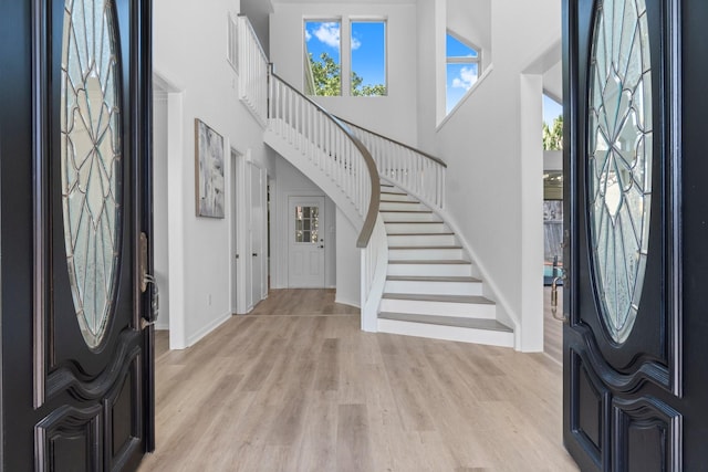 entryway featuring stairway, baseboards, light wood-style flooring, and a towering ceiling