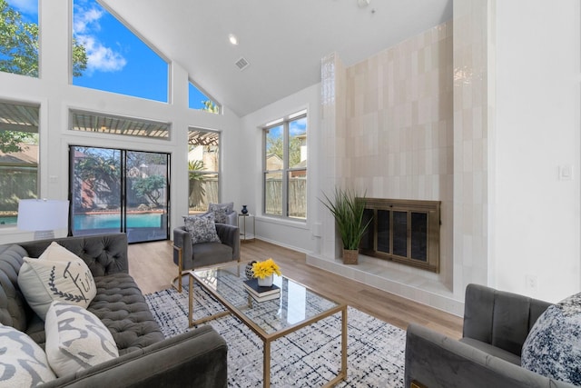 living room featuring a tiled fireplace, wood finished floors, visible vents, and high vaulted ceiling