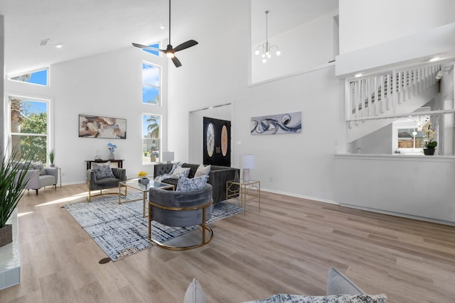 living area with wood finished floors, baseboards, high vaulted ceiling, stairs, and ceiling fan with notable chandelier