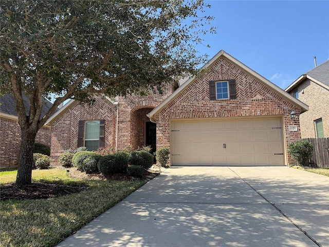 view of front of home featuring driveway, an attached garage, fence, and brick siding