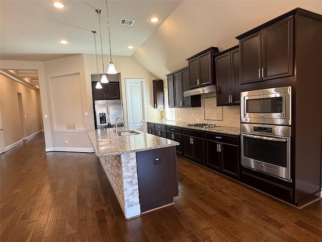 kitchen with light stone counters, under cabinet range hood, a sink, appliances with stainless steel finishes, and decorative backsplash