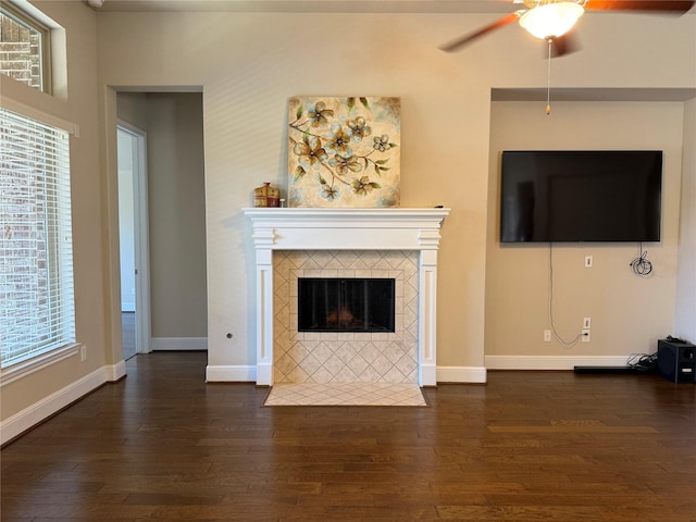 unfurnished living room featuring a ceiling fan, baseboards, dark wood-style flooring, and a tile fireplace