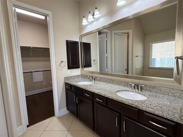 bathroom with baseboards, double vanity, a sink, and tile patterned floors