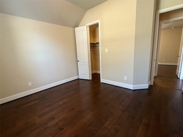 unfurnished bedroom with lofted ceiling, dark wood-type flooring, baseboards, a closet, and a walk in closet