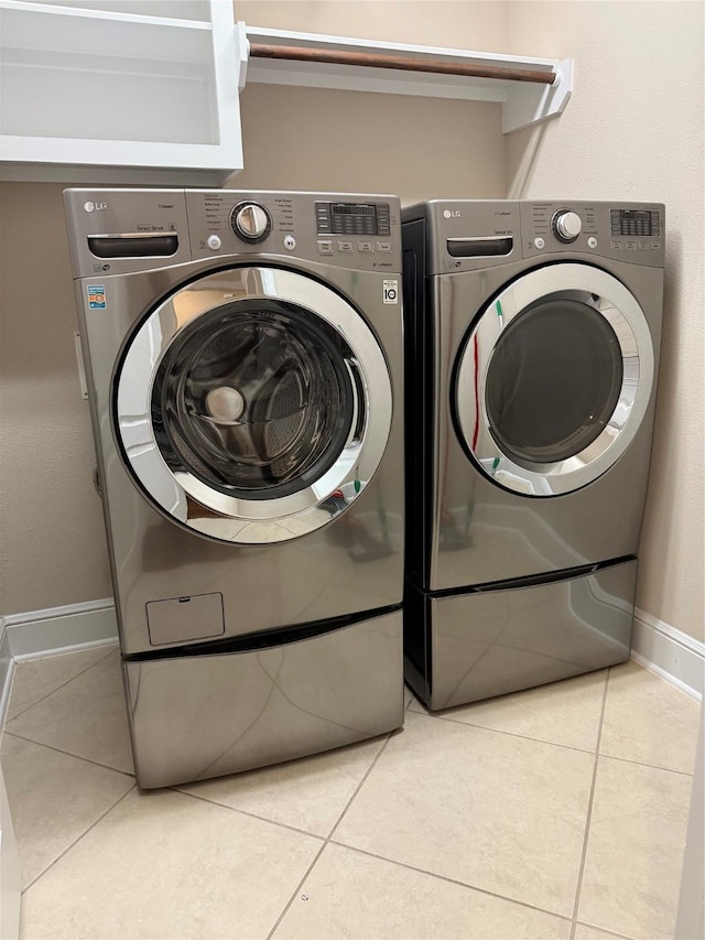 clothes washing area with laundry area, light tile patterned flooring, washer and clothes dryer, and baseboards