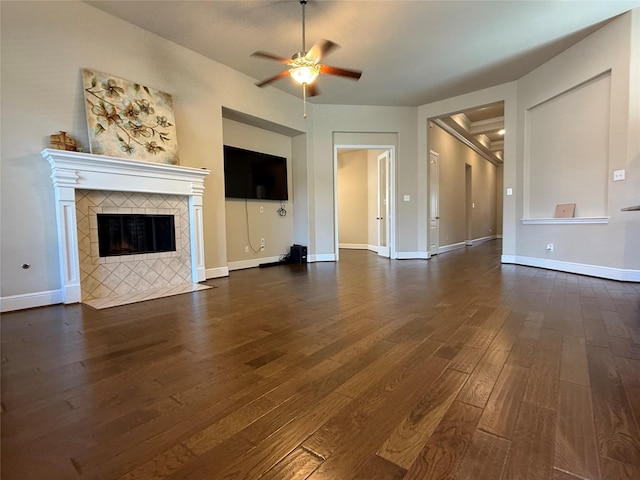 unfurnished living room featuring dark wood-type flooring, a tile fireplace, ceiling fan, and baseboards