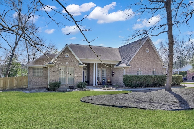 view of front of house featuring a shingled roof, fence, a front lawn, and brick siding