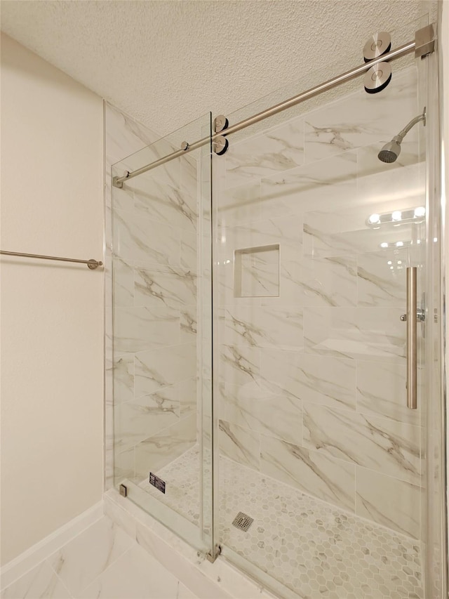 bathroom with a textured ceiling, marble finish floor, a marble finish shower, and baseboards